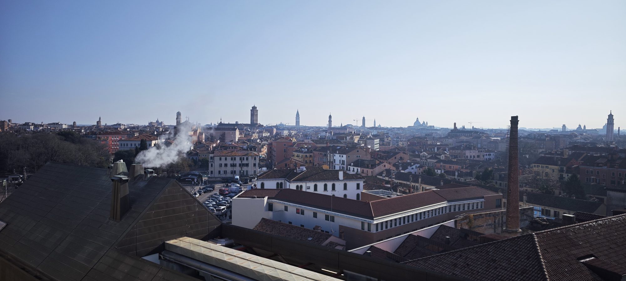 Vista panorámica desde los tejados de Venecia con humo saliendo de una chimenea.