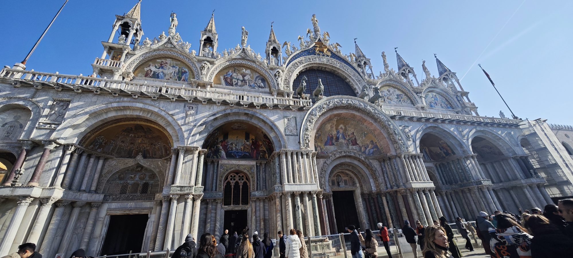 Fachada detallada de la Basílica de San Marcos en Venecia bajo un cielo azul despejado.