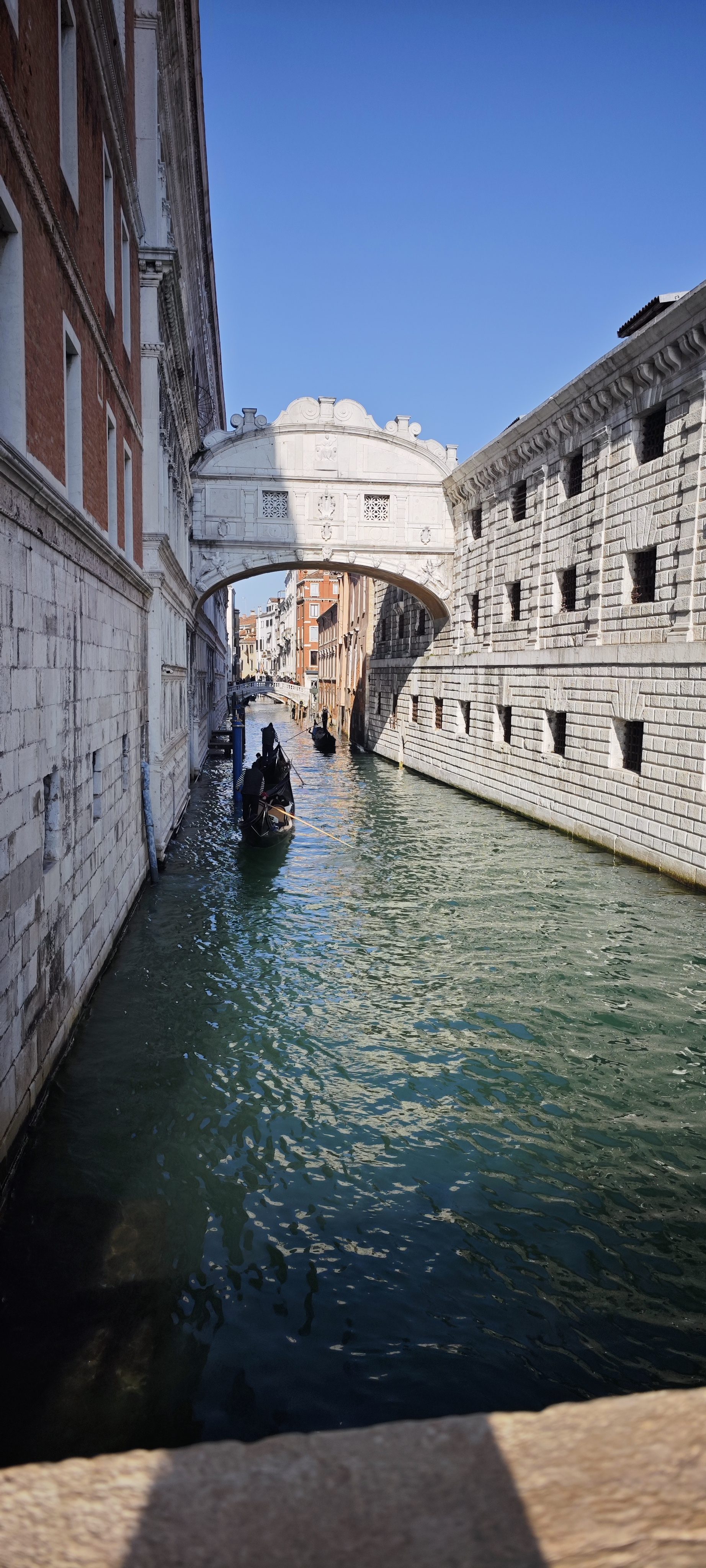 Góndola navegando por un canal de agua verde bajo el Puente de los Suspiros en Venecia.