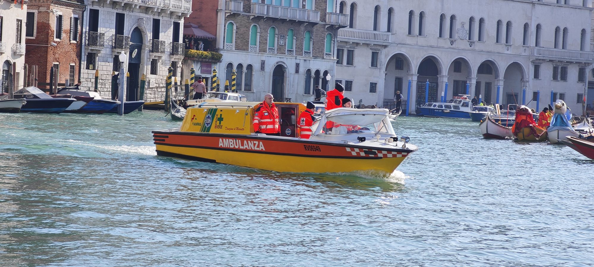 Barco ambulancia amarillo navegando por un canal rodeado de edificios históricos en Venecia.
