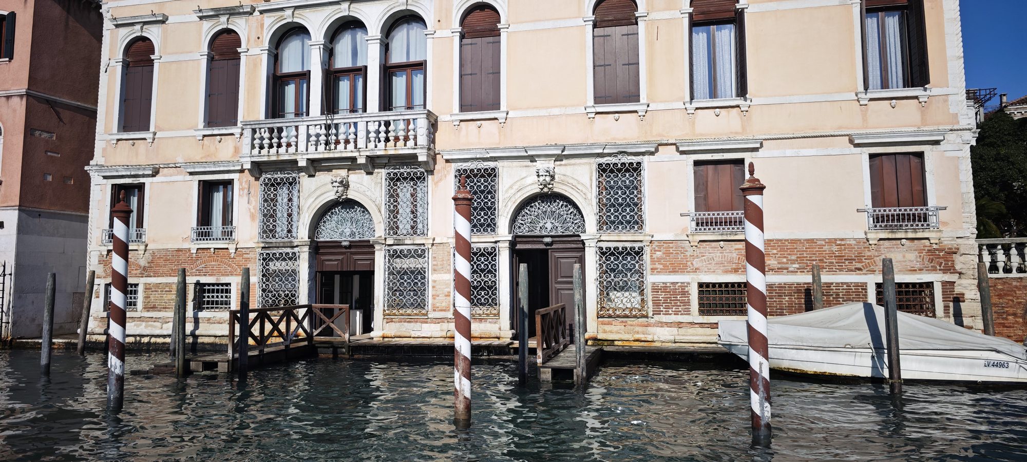 Fachada de un palacio histórico veneciano junto al agua con postes de amarre tradicionales.