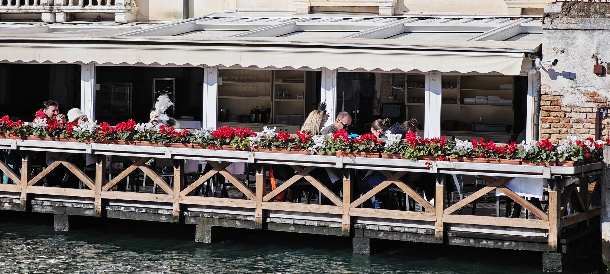 Terraza sobre un canal de Venecia decorada con flores y persona luciendo máscara carnavalesca.