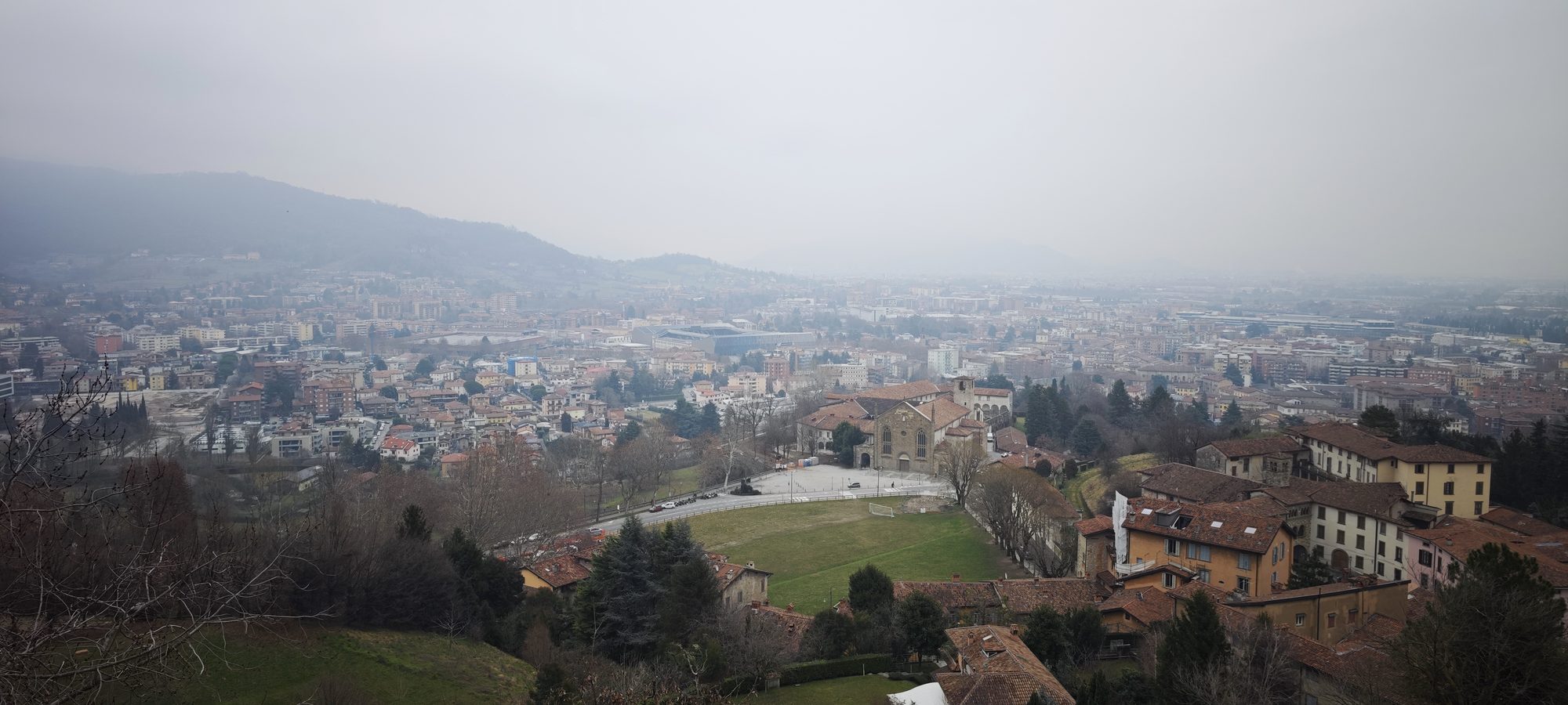 Vista panorámica de Torre Boldone y sus colinas bajo un cielo brumoso de invierno.