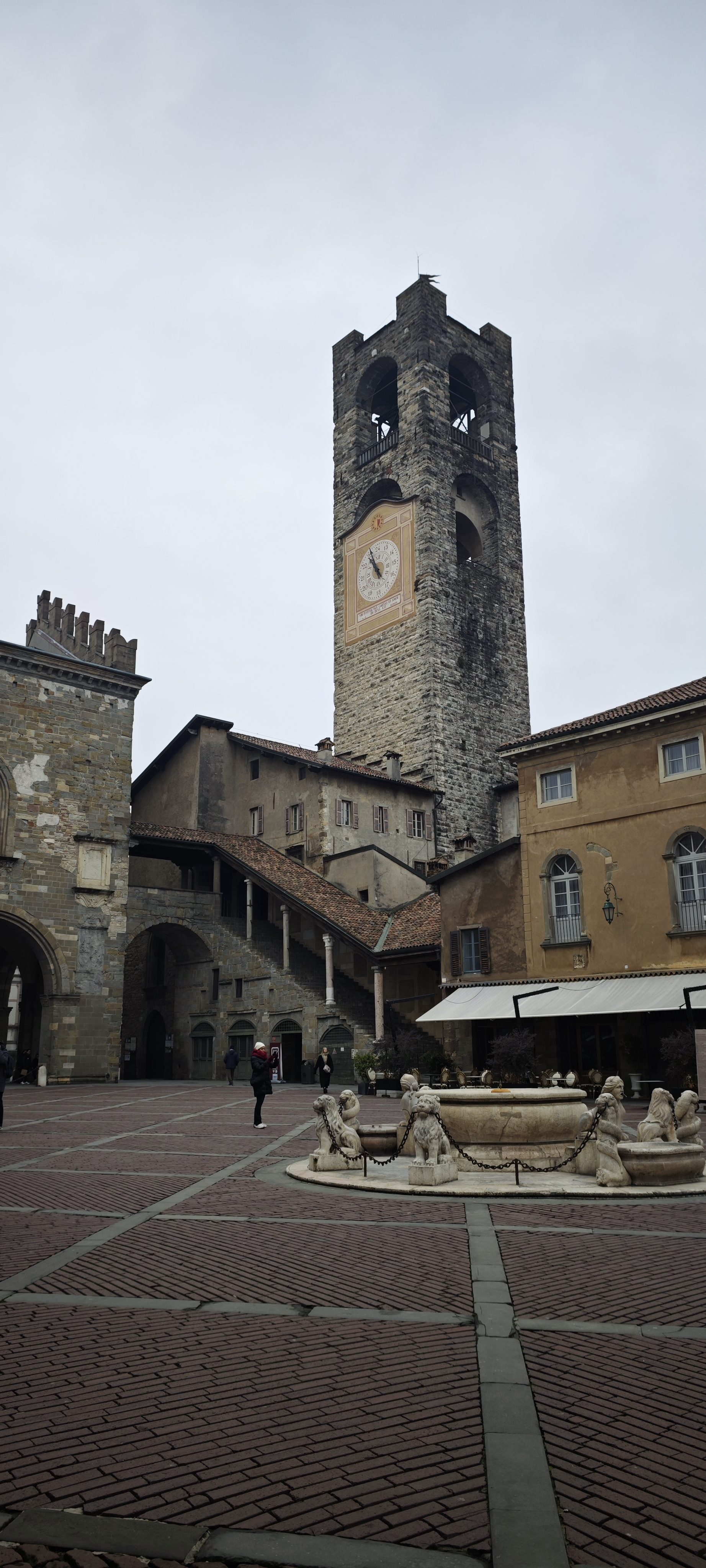 Torre medieval del reloj y fuente de piedra en la Piazza Vecchia de Bérgamo.