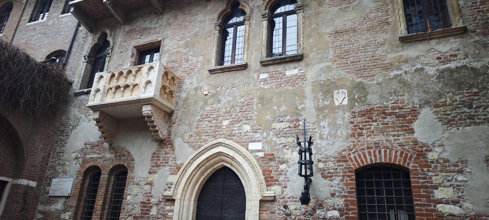 Fachada de ladrillo medieval con el célebre balcón de piedra tallada de Julieta.