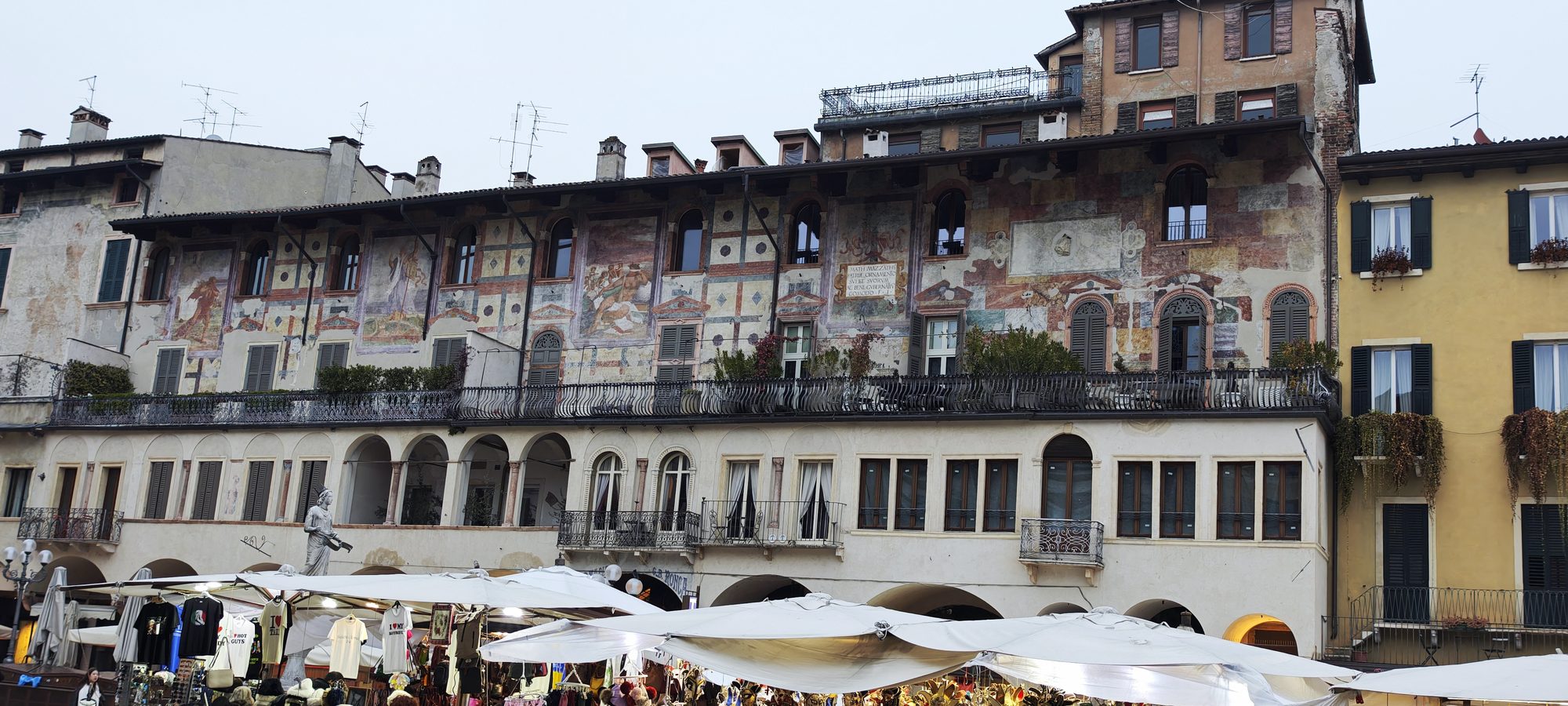 Fachada de edificio histórico con frescos renacentistas y puestos de mercado en Verona.