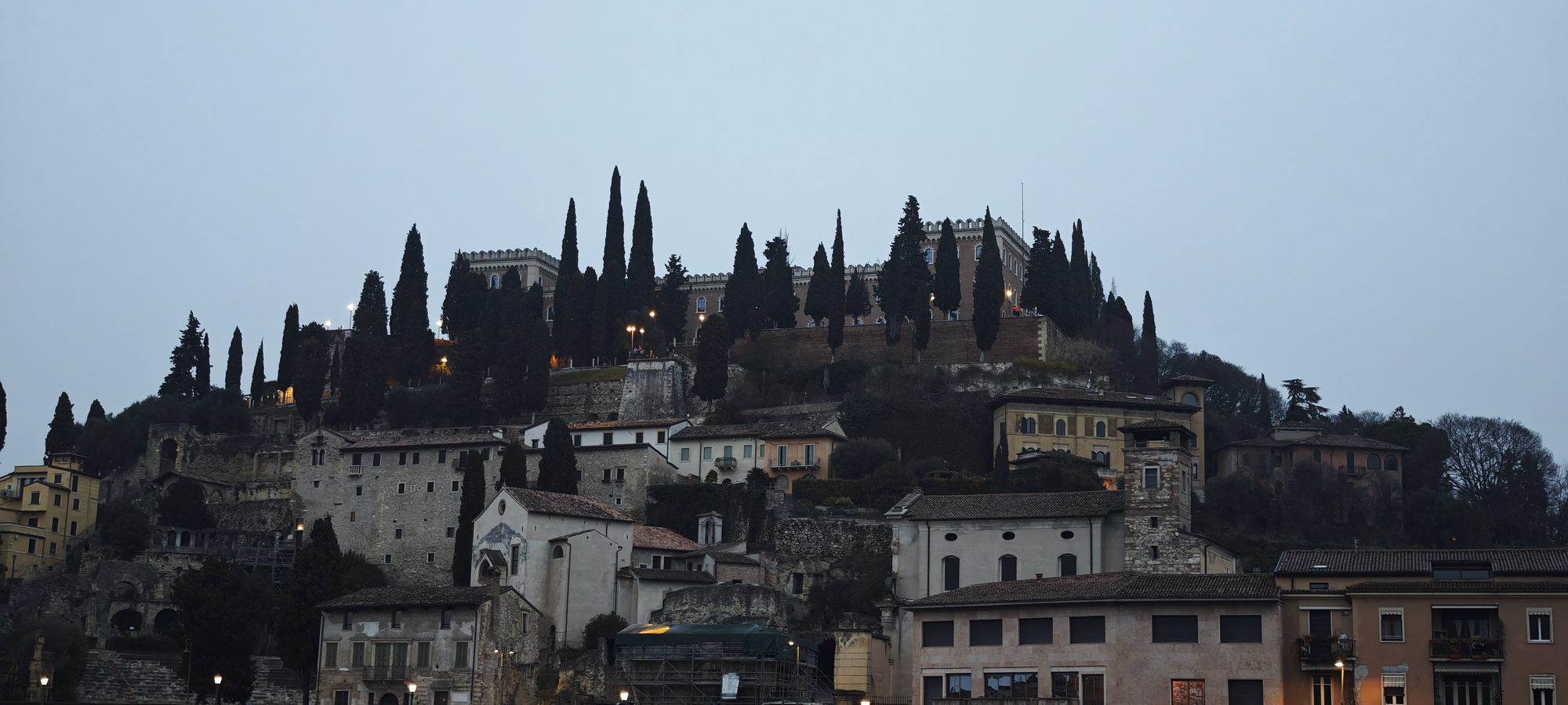 Colina en Verona con edificios históricos de piedra y cipreses al anochecer.