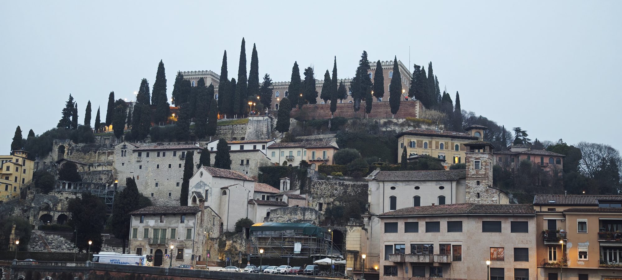 Colina de Castel San Pietro en Verona con edificios históricos y cipreses al anochecer.
