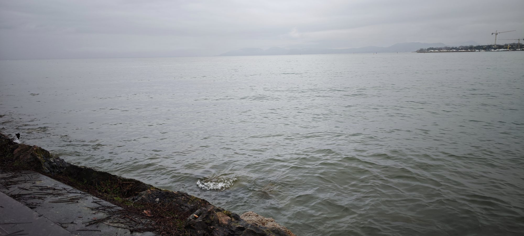 Aguas del Lago de Garda bajo un cielo nublado con montañas en el horizonte.