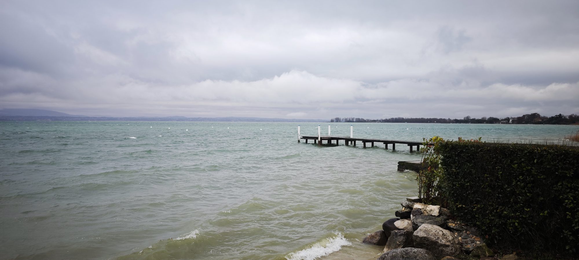 Muelle de madera sobre el agua turquesa del lago bajo un cielo nublado.