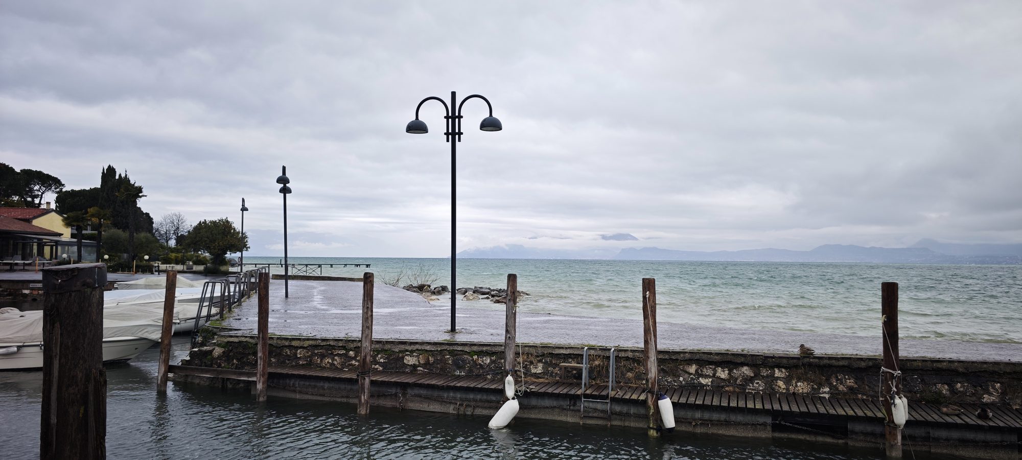 Muelle de piedra con farolas a orillas del lago bajo un cielo nublado.