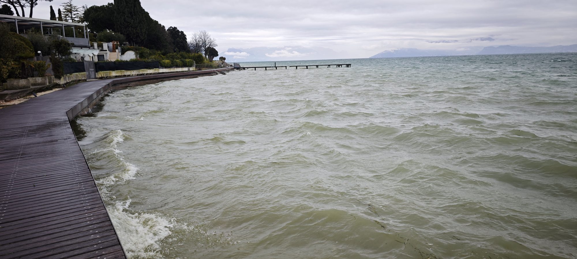 Pasarela de madera junto al lago picado bajo un cielo nublado en Sirmione.