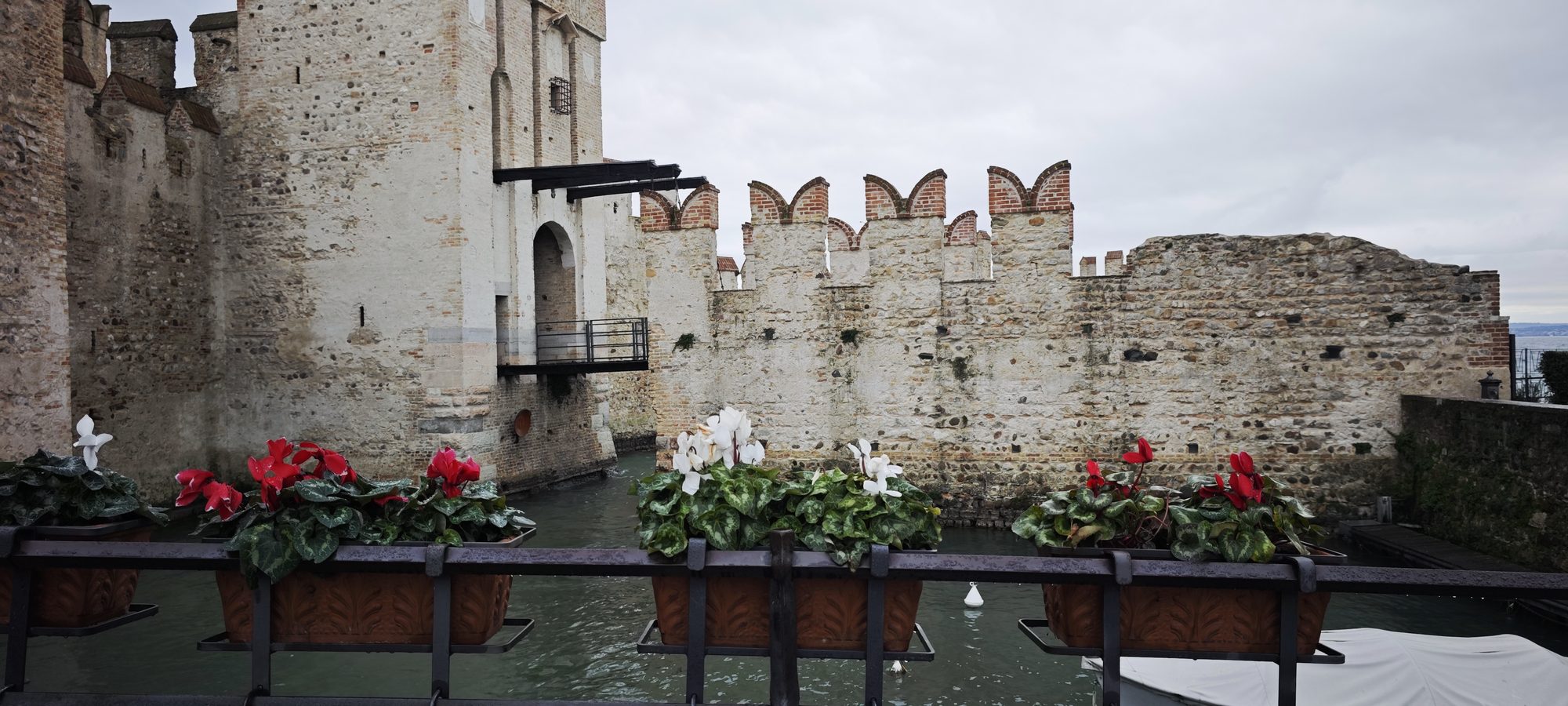 Castillo medieval de Sirmione junto al agua con jardineras de ciclámenes en primer plano.