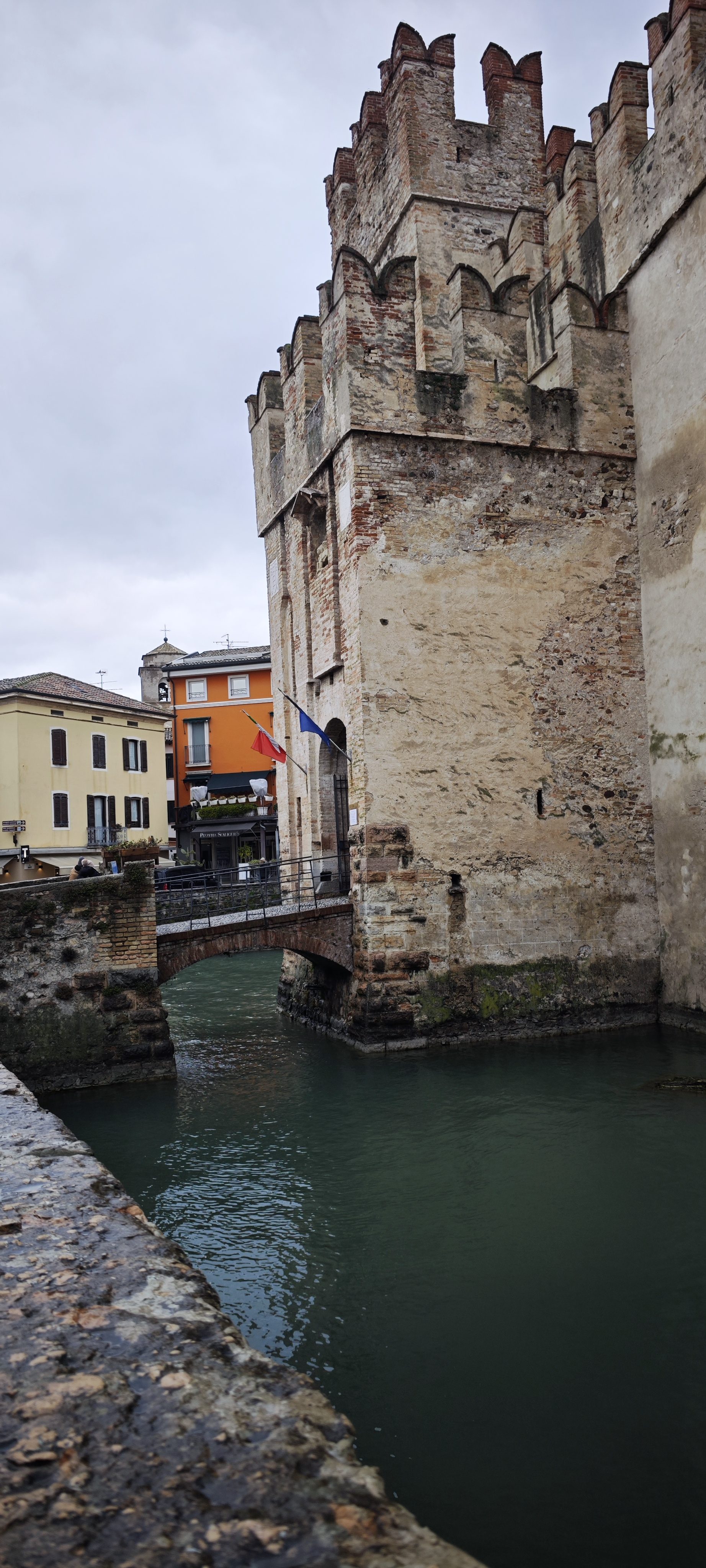 Castillo medieval de piedra sobre el agua con puente de arco en Sirmione.