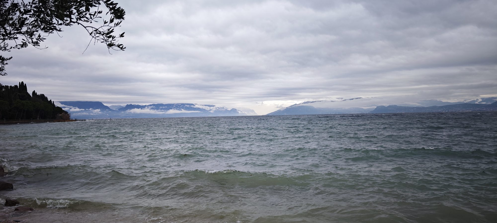 Lago de Garda agitado en Sirmione bajo un cielo nublado y montañas al fondo.