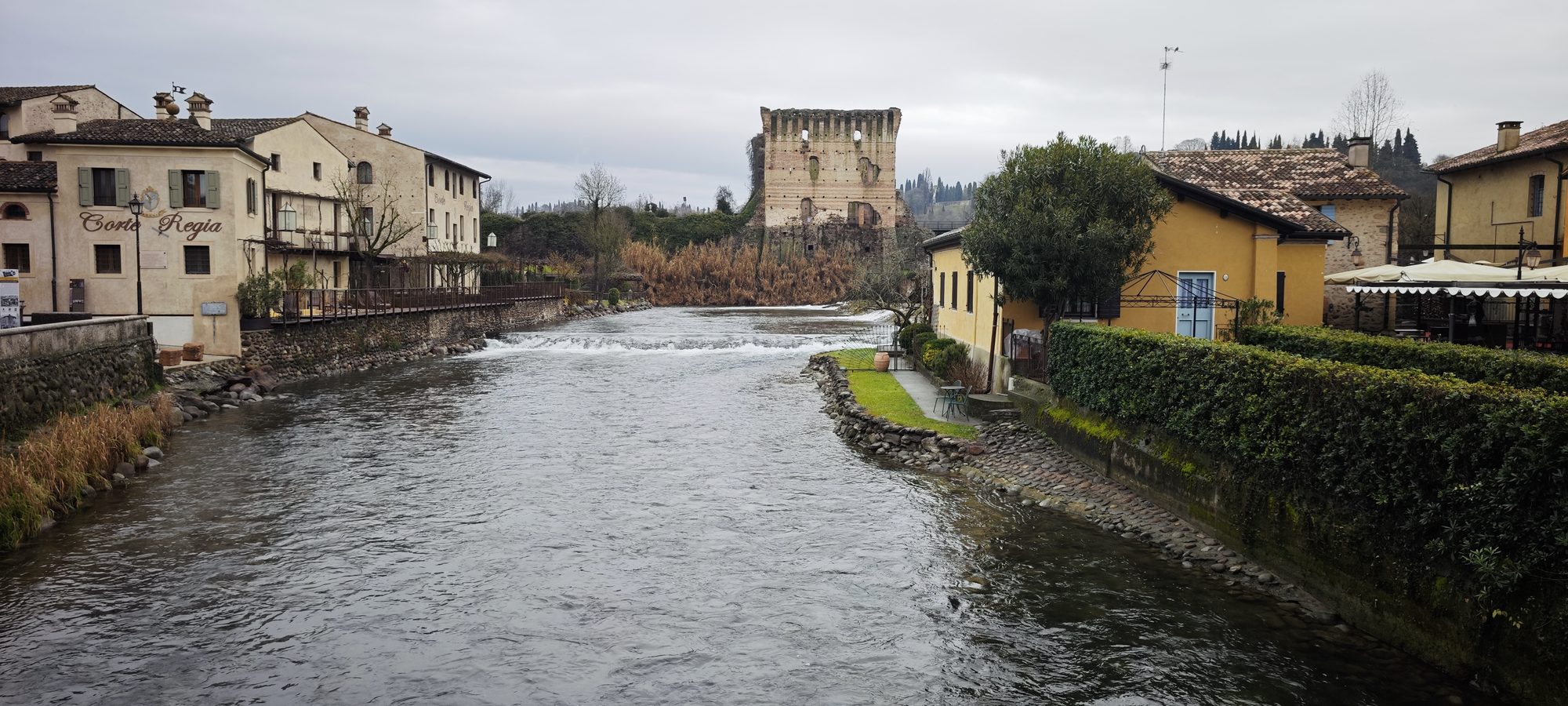 Río Mincio fluyendo entre casas históricas de piedra y ruinas de una torre en Valeggio.