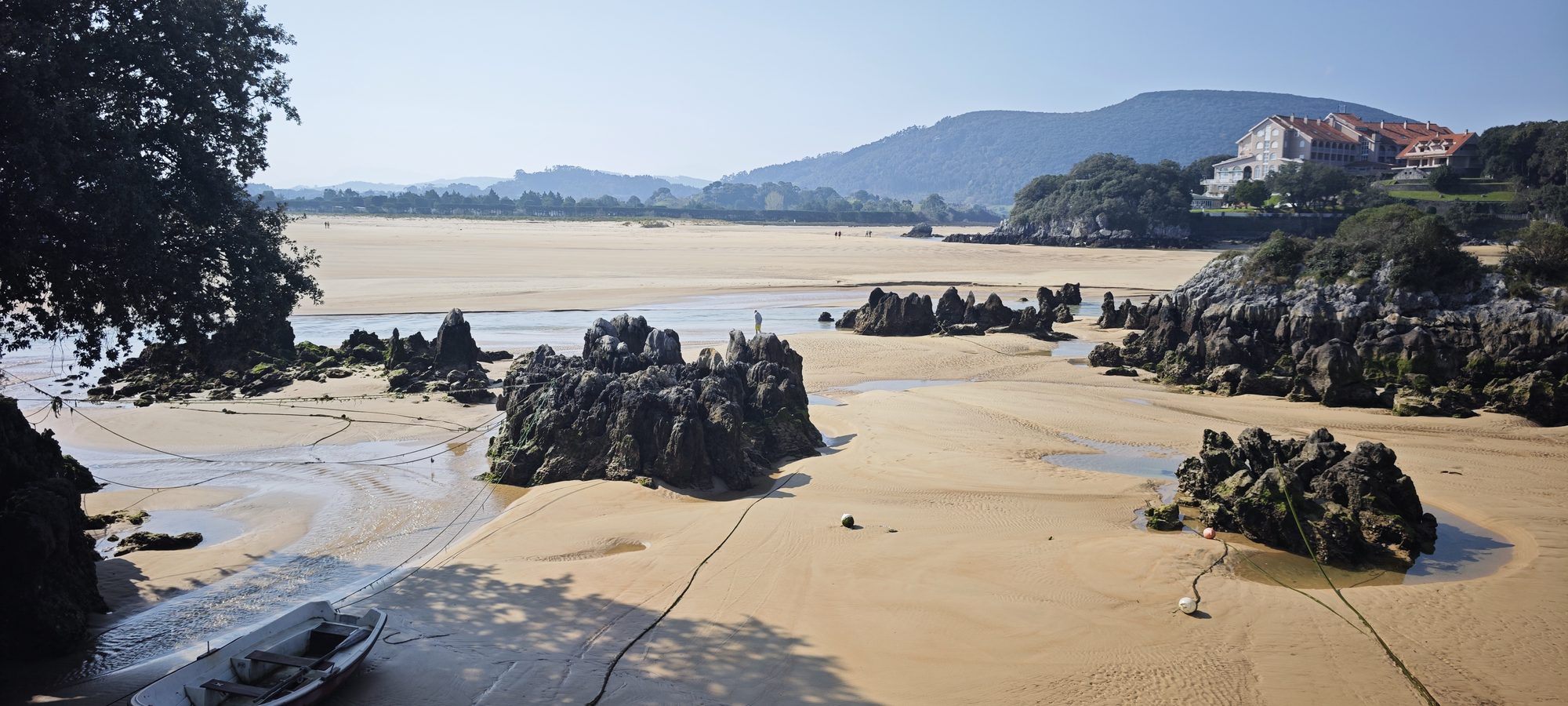 Playa de arena dorada con formaciones rocosas oscuras y una pequeña barca en la orilla.