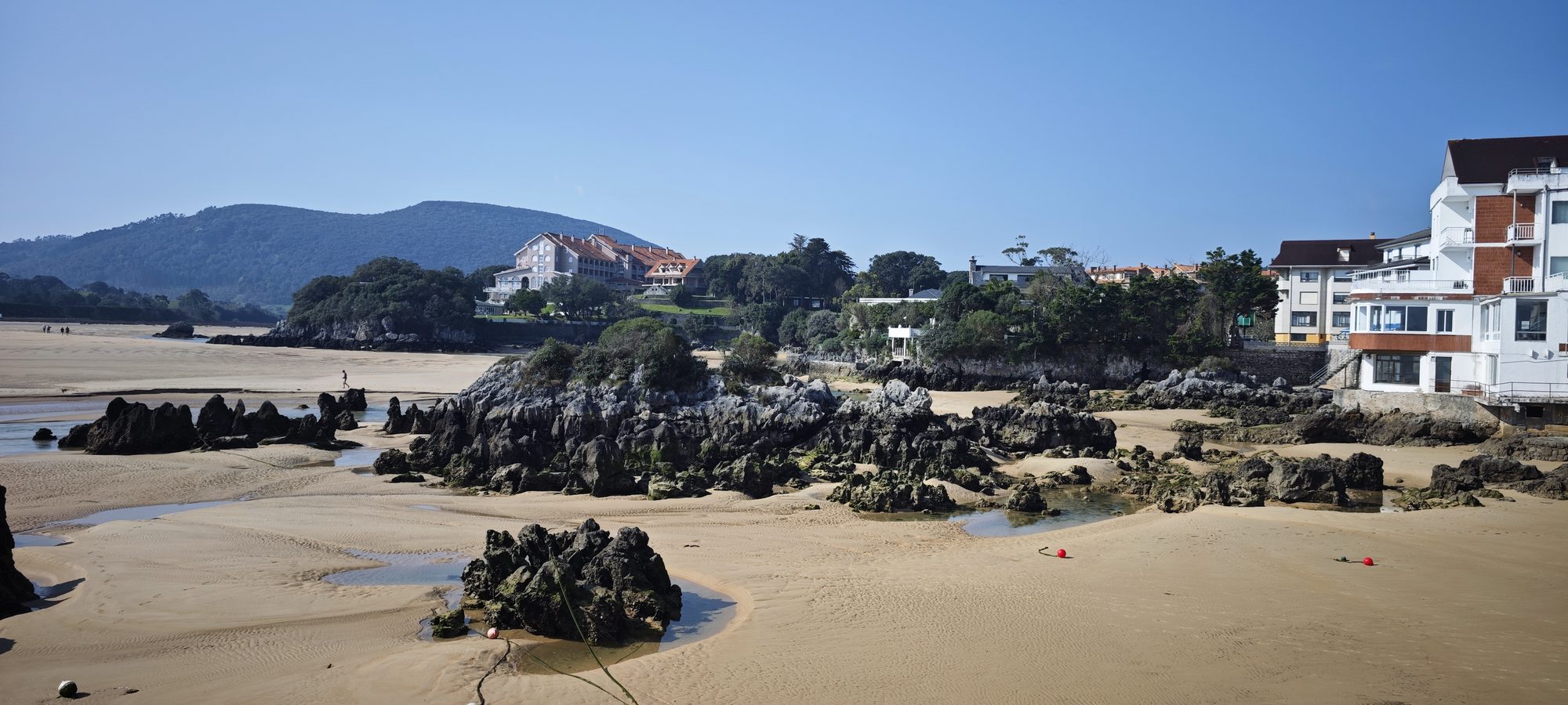 Playa de arena y rocas con edificios costeros y montañas en Arnuero, Cantabria.