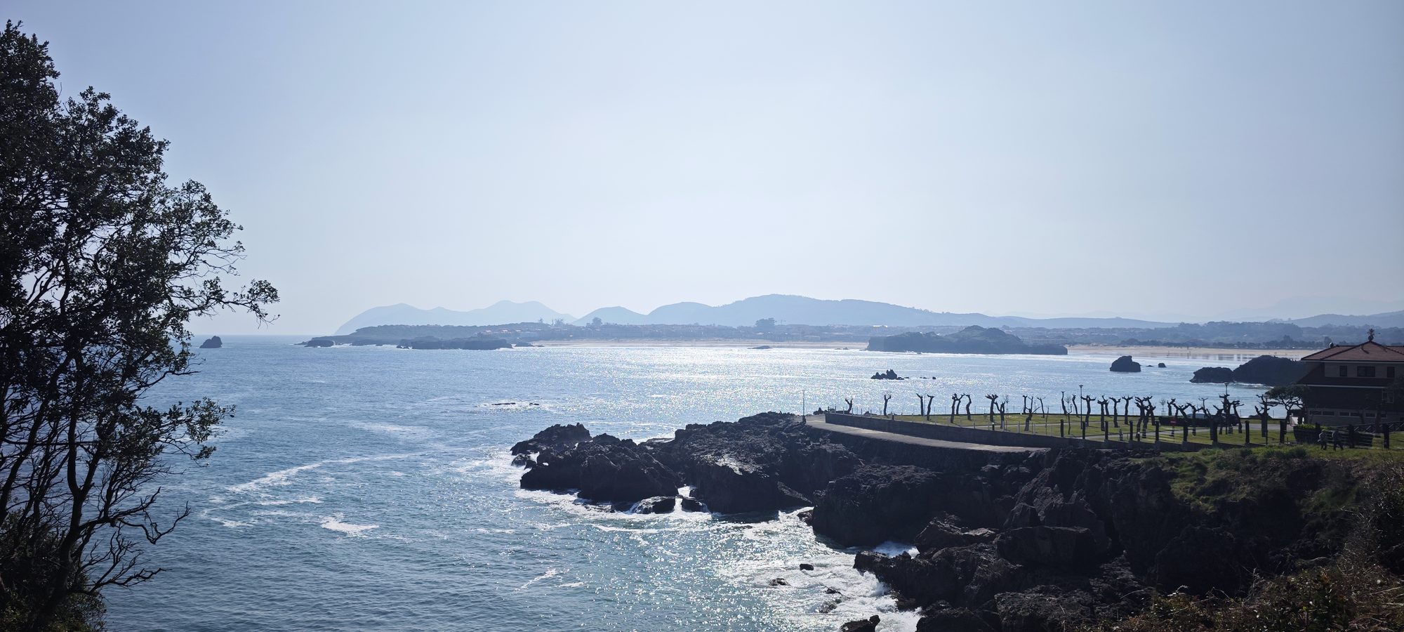 Acantilados rocosos y mar Cantábrico bajo la luz del sol reflejándose en el agua.