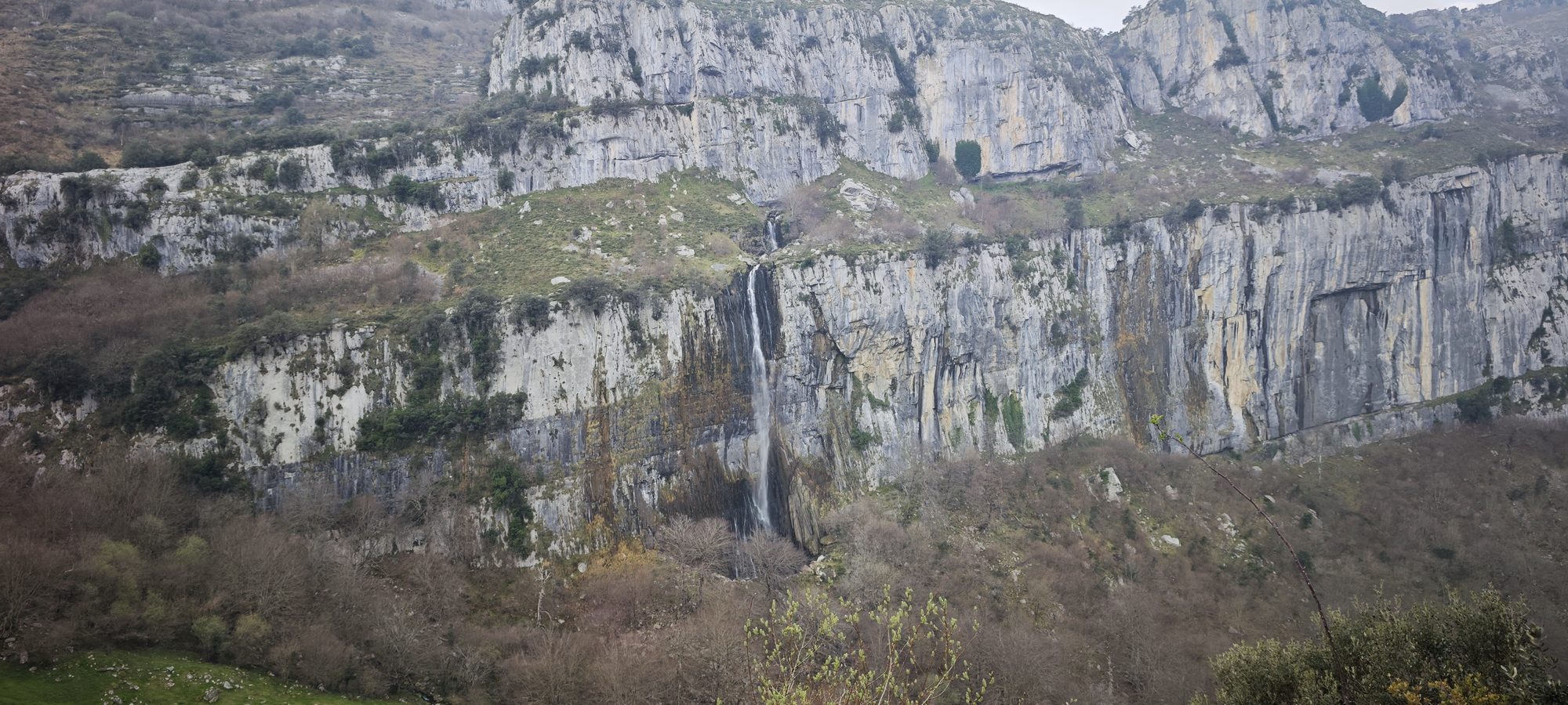 Gran cascada cayendo por un acantilado rocoso rodeado de vegetación y montañas.