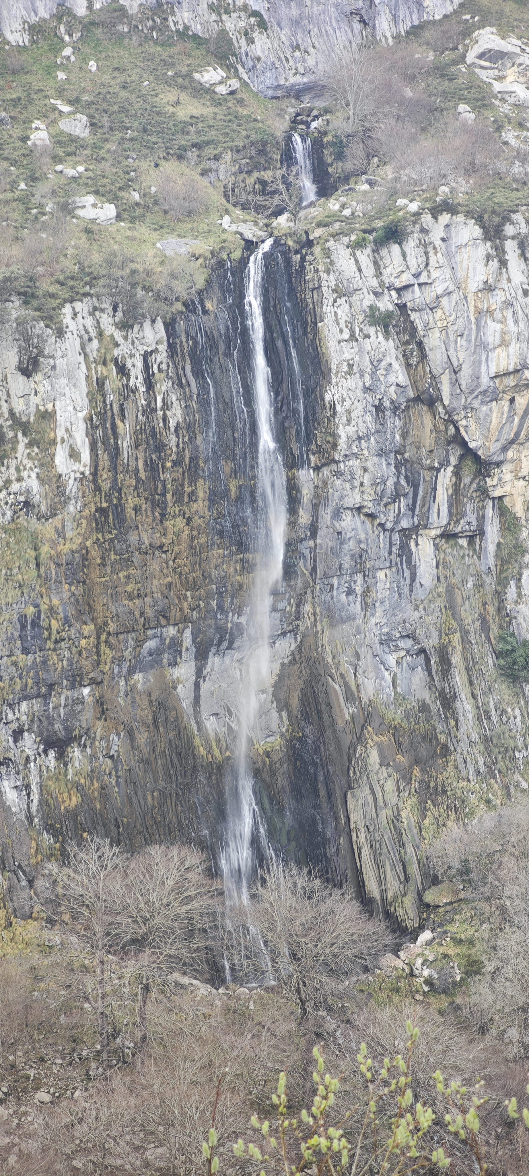 Gran cascada cayendo por una alta pared rocosa en un entorno de montaña.