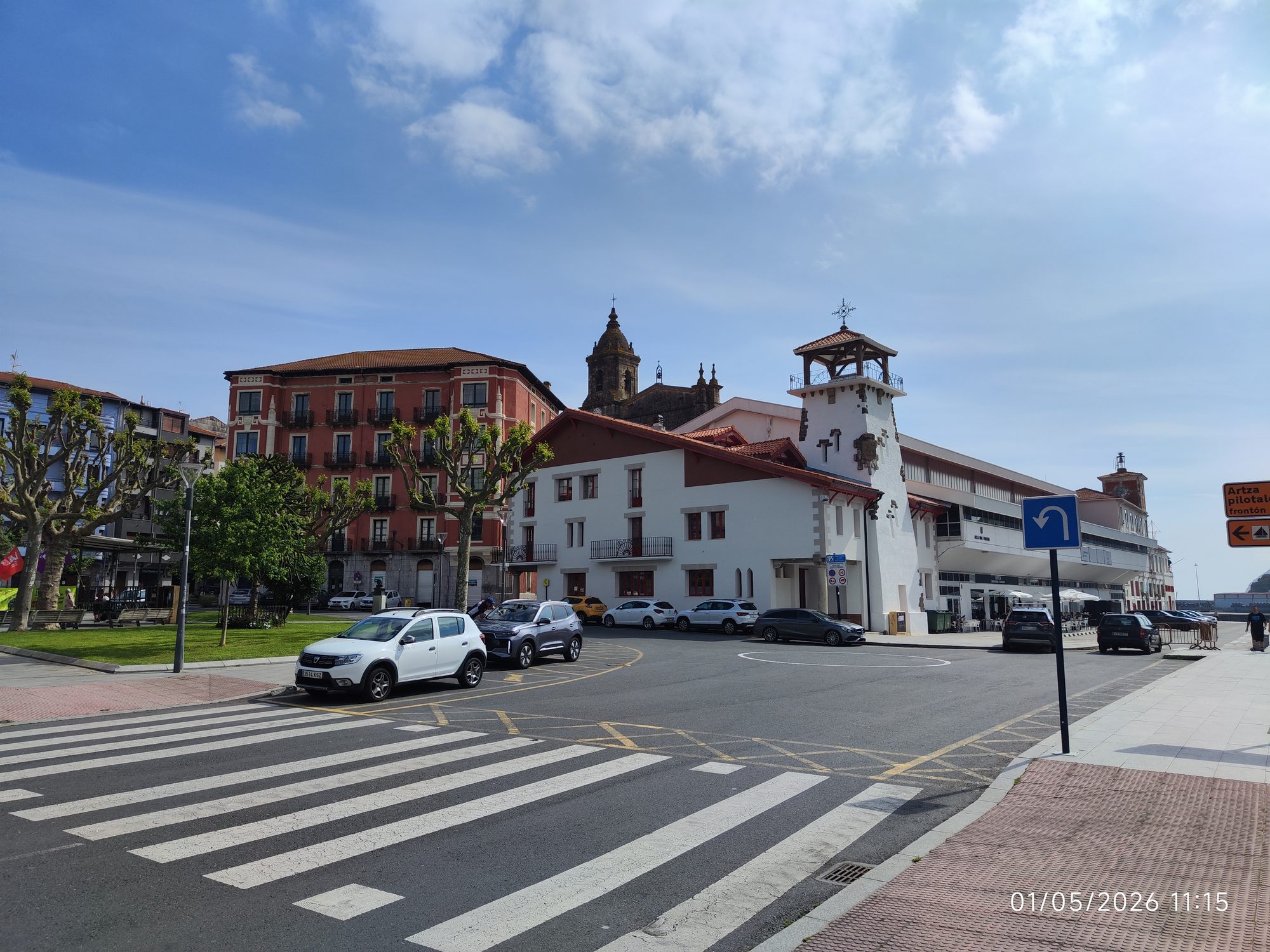 Plaza con edificios tradicionales, paso de peatones y coches bajo un cielo despejado en Bermeo.
