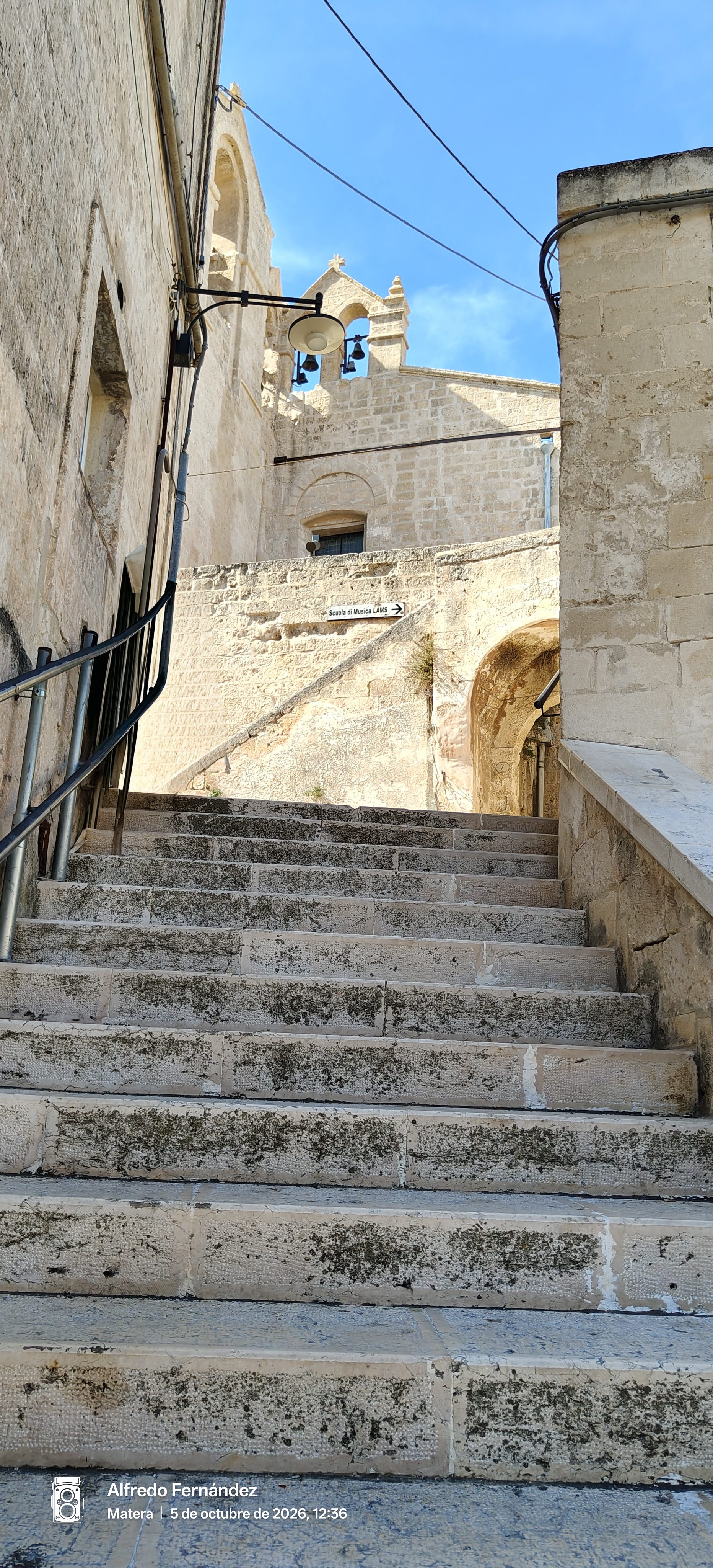 Escalera empinada de piedra que asciende entre edificios históricos hacia un campanario en Matera.