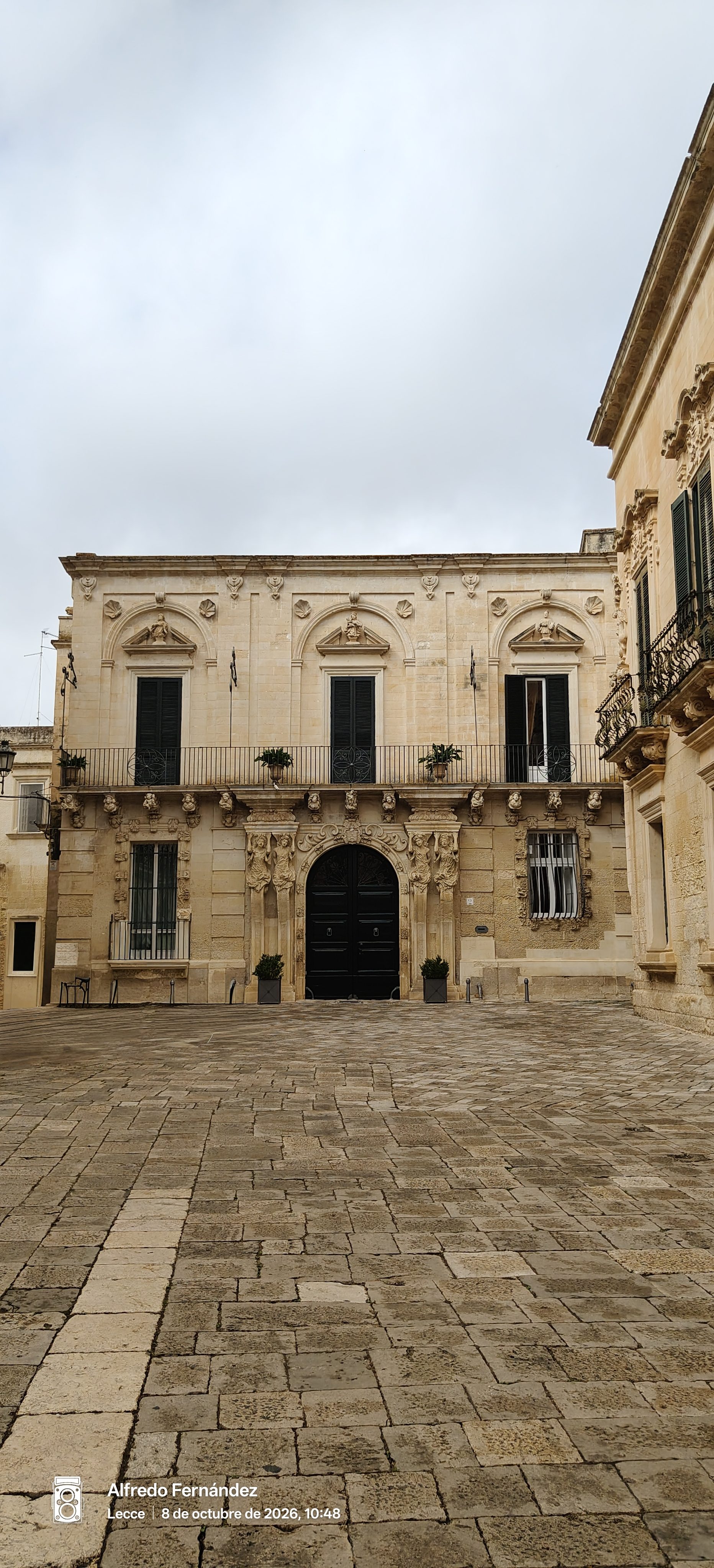 Fachada de palacio barroco de piedra caliza frente a plaza adoquinada en Lecce.