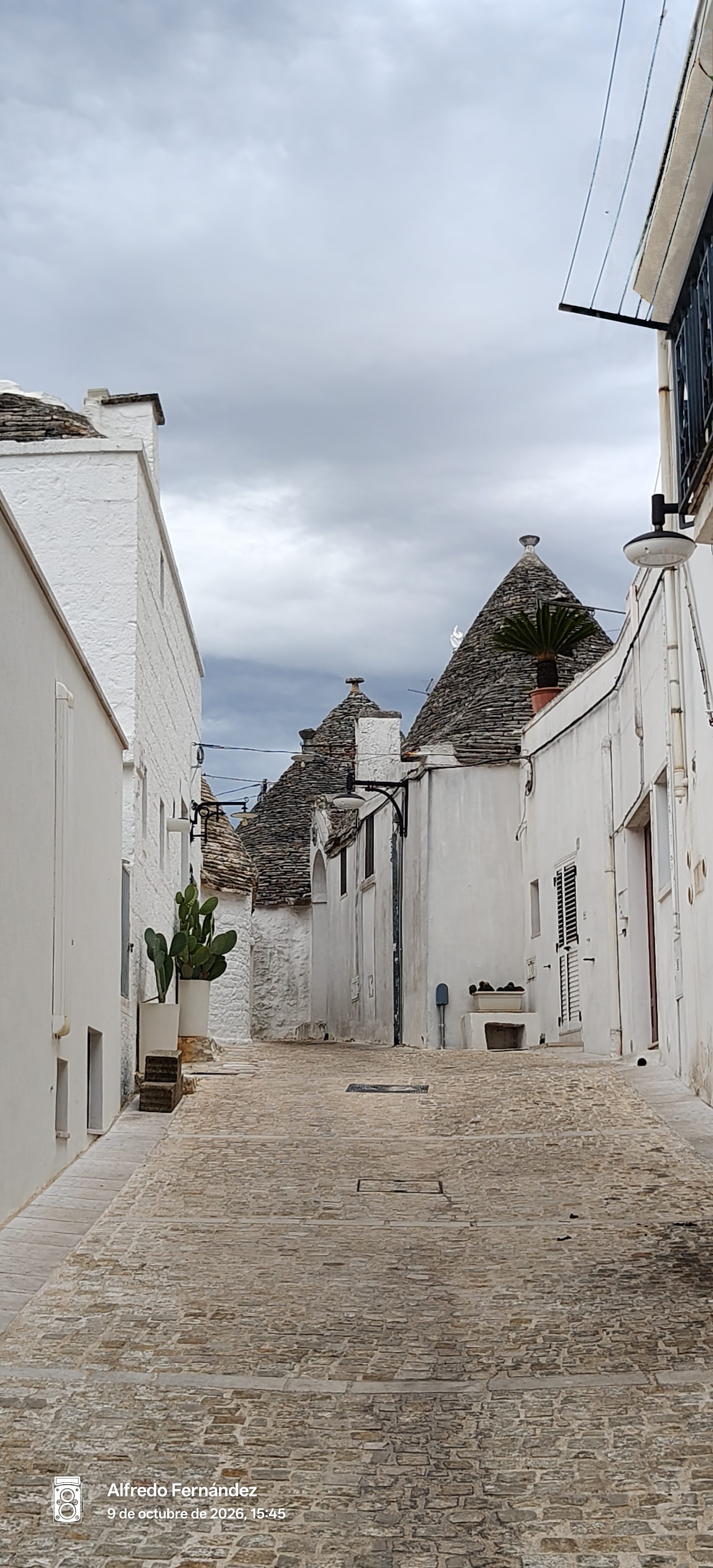Callejón empedrado flanqueado por casas trulli de paredes blancas y techos cónicos en Alberobello.