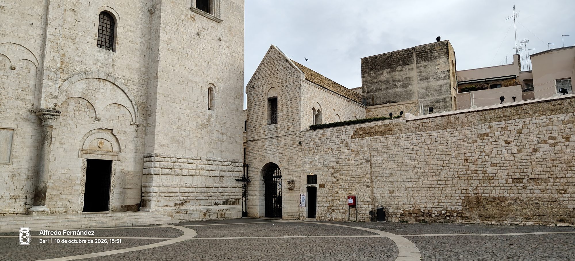 Fachada románica de piedra caliza blanca frente a una plaza adoquinada en Bari.